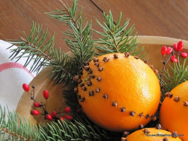 An orange clove pomander setting in a bowl with winter greenery.