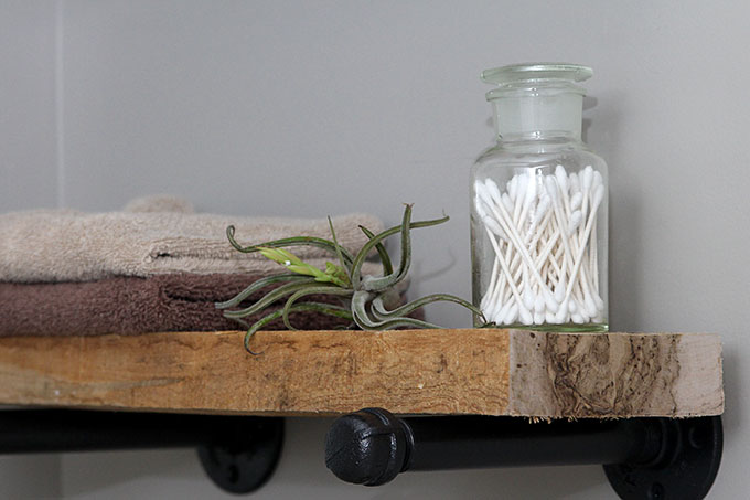 DIY industrial pipe shelving in bathroom topped with air plant, towels, and q-tips