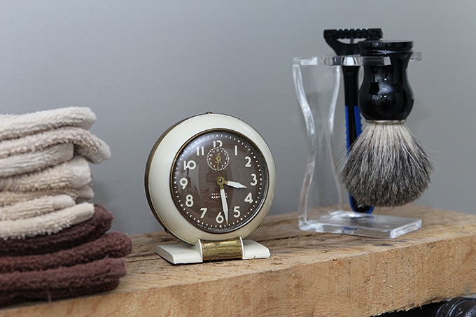 diy pipe shelf topped with shaving brush, razor, washcloths, and clock