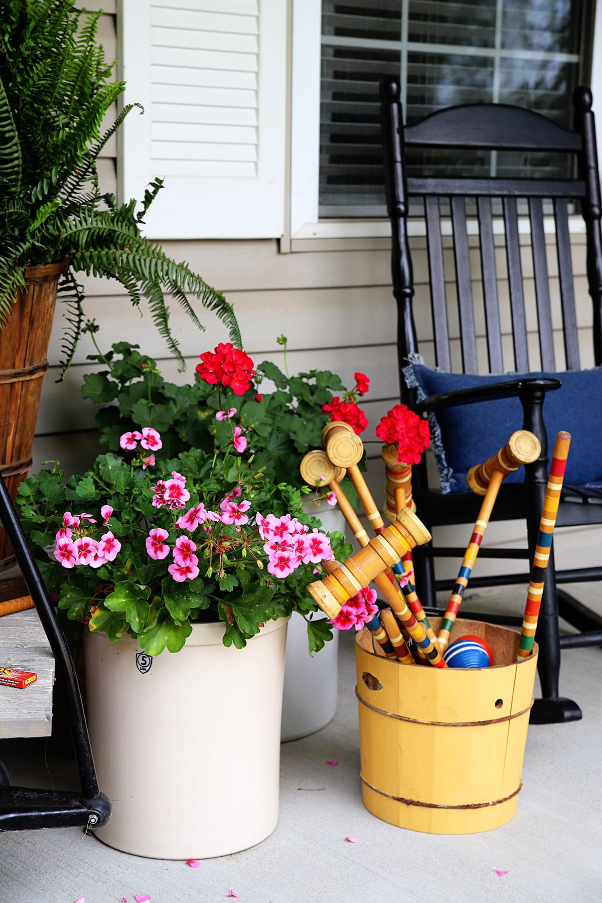 Geraniums planted in crocks on the front porch. Croquet set in a yellow ice cream churn to the side. 