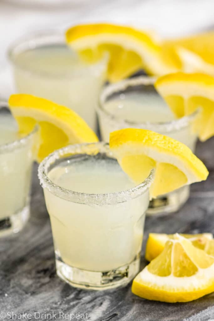 Glasses of yellow colored lemon drop shots with a slice of lemon as a garnish.