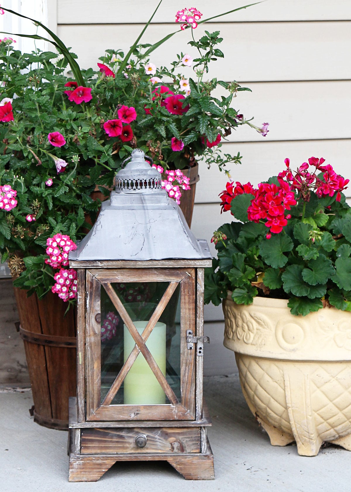 Wooden lantern featured on a small porch with a pink potted flowers. 