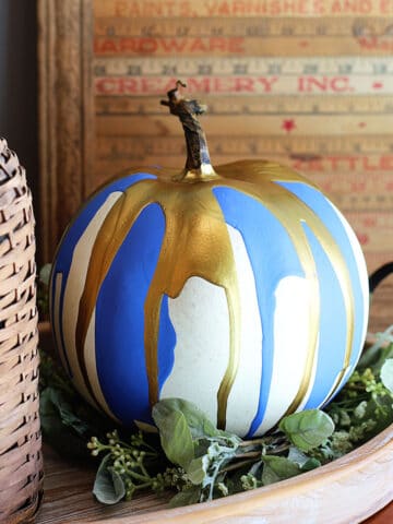 Pumpkin decorated by the paint pouring technique setting on a tray surrounded by rustic farmhouse decor.