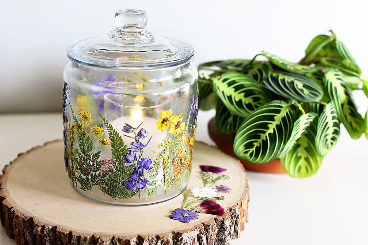 Glass jar with pressed flowers decoupaged onto it with a flickering candle inside. All setting on a wood slice. 