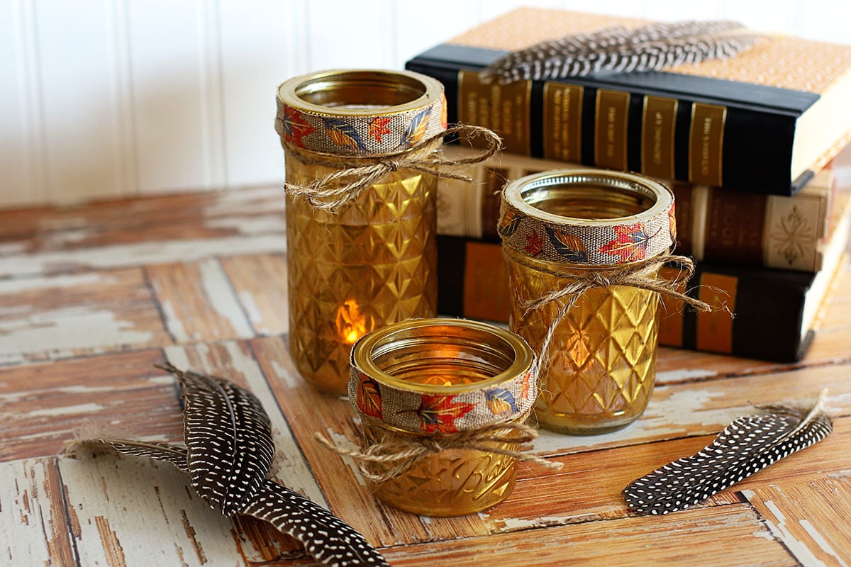Gold painted mason jars used as votive holders displayed with feathers and books.