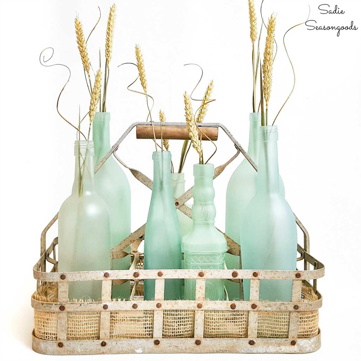 6 repurposed bottles painted in the color sea glass and sitting in a bottle carrier.