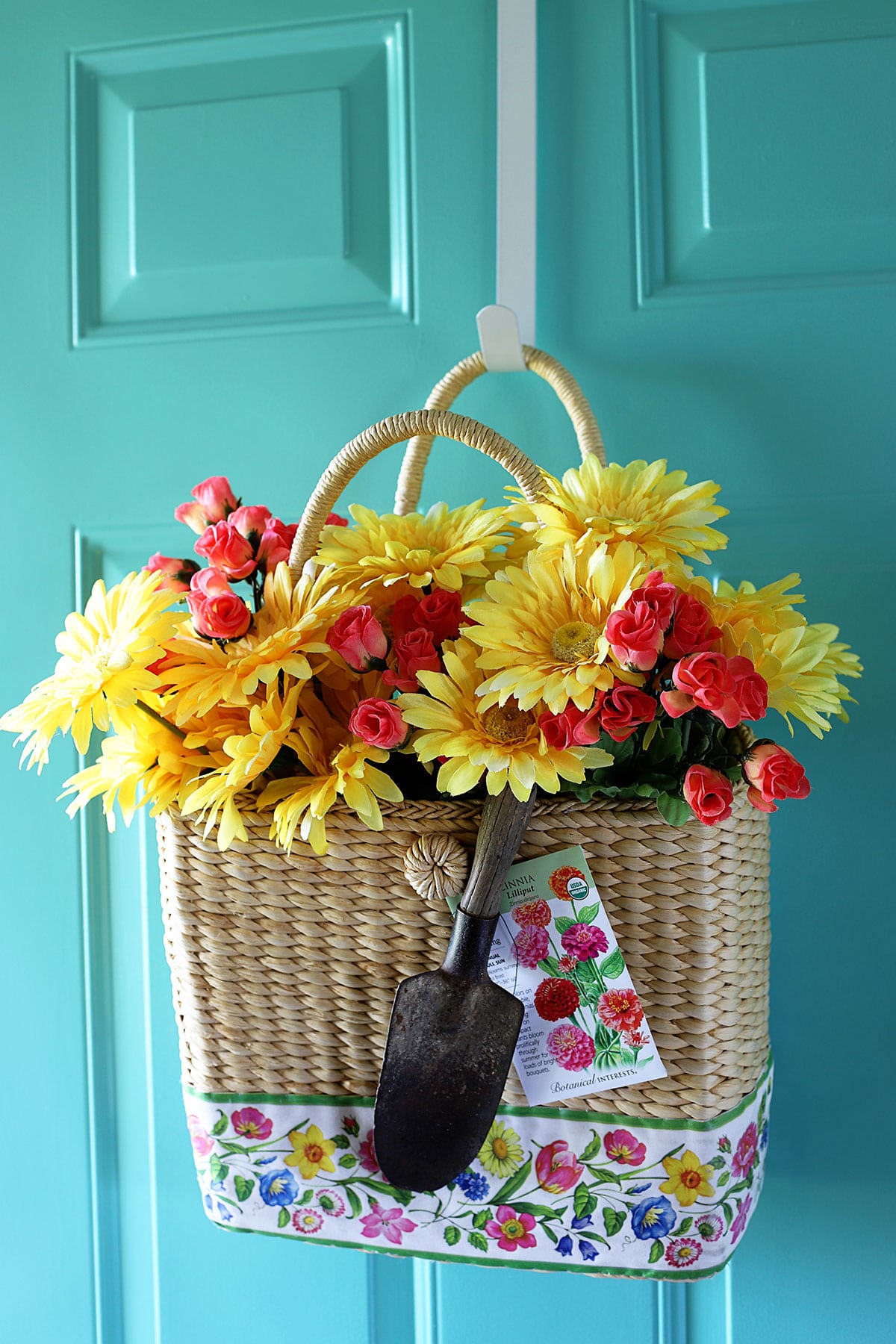 A straw purse hung as a wreath on a door with yellow daisies and bright pink roses.