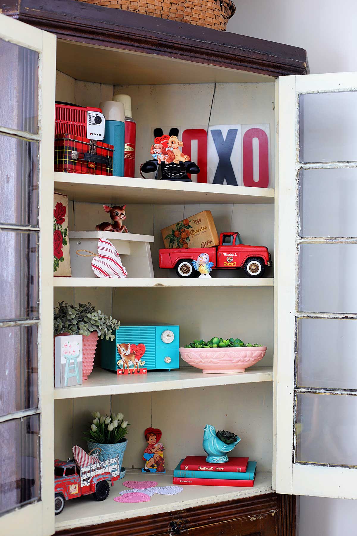 cabinet filled with vintage pottery, red trucks, classroom Valentines and more thrift store finds